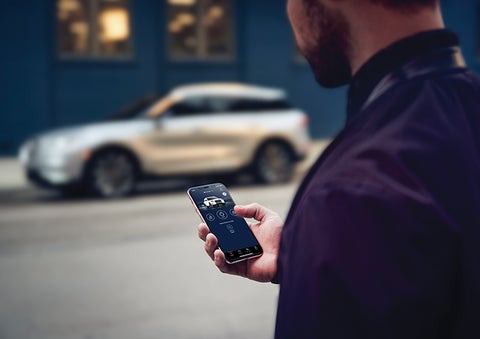 A person is shown interacting with a smartphone to connect to a Lincoln vehicle across the street. | Parks Lincoln of Tampa in Tampa FL