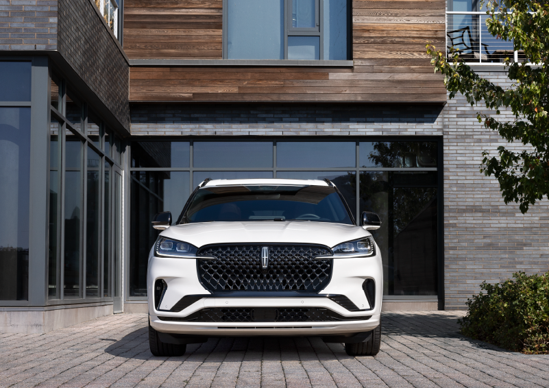 A white 2025 Lincoln Aviator® SUV is shown parked outside a modern building with gray brick and wood accents. | Parks Lincoln of Tampa in Tampa FL