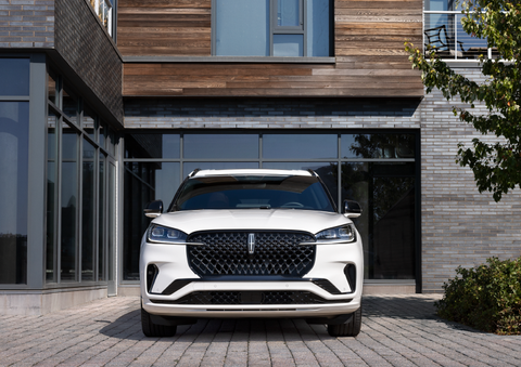 A white 2025 Lincoln Aviator® SUV is shown parked outside a modern building with gray brick and wood accents. | Parks Lincoln of Tampa in Tampa FL