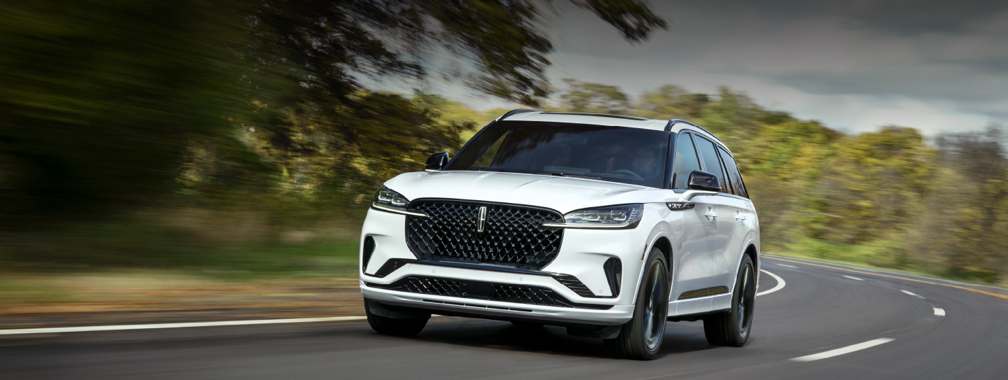 A white 2025 Lincoln Aviator® SUV is being driven down a road lined with trees. | Parks Lincoln of Tampa in Tampa FL