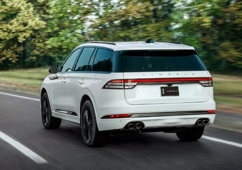 A white 2026 Lincoln Aviator® SUV is being driven away down a road lined with colorful trees. | Parks Lincoln of Tampa in Tampa FL