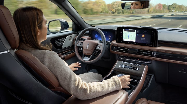 A 2026 Lincoln Aviator® SUV is being driven hands-free on a highway near a forest | Parks Lincoln of Tampa in Tampa FL