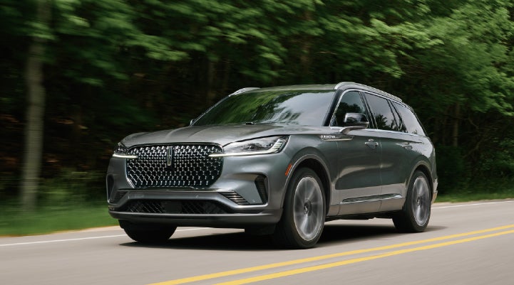 A 2027 Lincoln Aviator® SUV is being driven down a road lined with trees. | Parks Lincoln of Tampa in Tampa FL